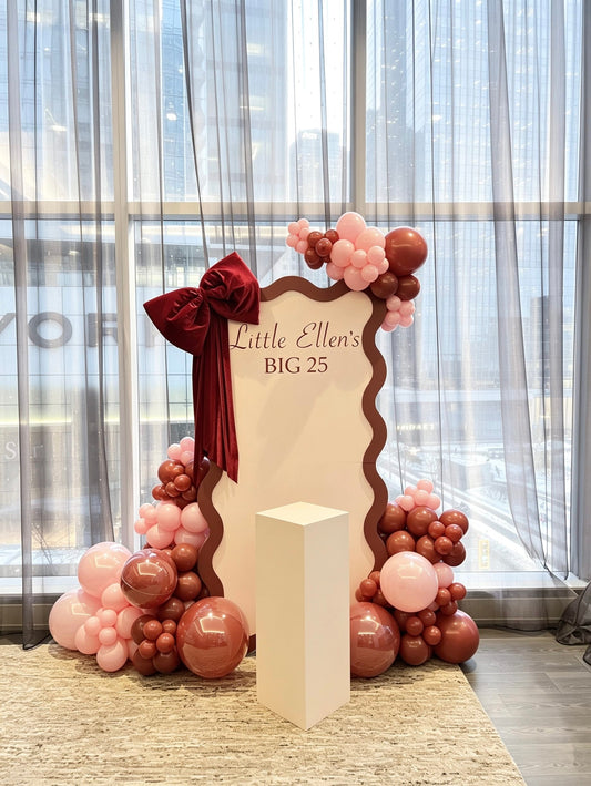 bow inspired birthday backdrop with blush balloon decor and oversized velvet bow