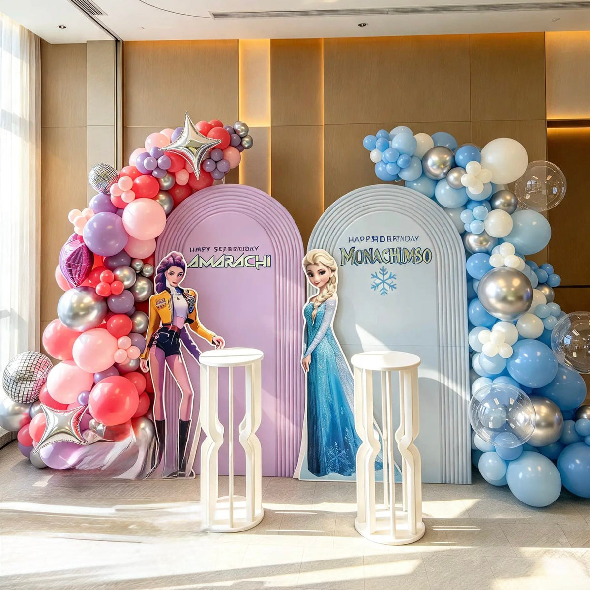 K-Pop Demon Hunters and Frozen double birthday backdrop with lavender and blue ripple arches, pink and blue balloon garlands, Elsa and K-Pop character cutouts, silver stars and white cake pedestals.