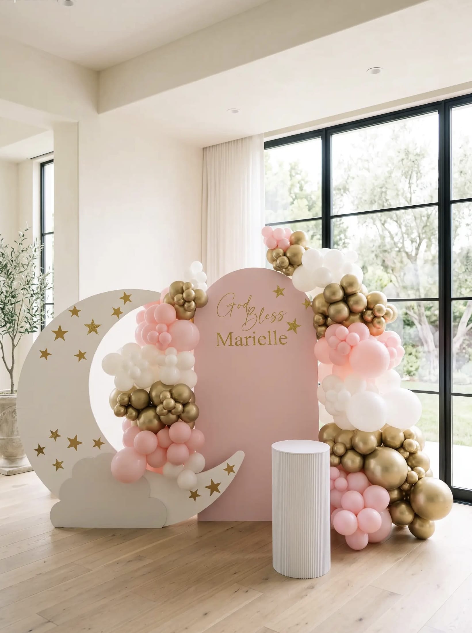Pink baptism backdrop with a white crescent moon, gold stars, blush pink, white and gold balloon garland and personalized God Bless lettering.