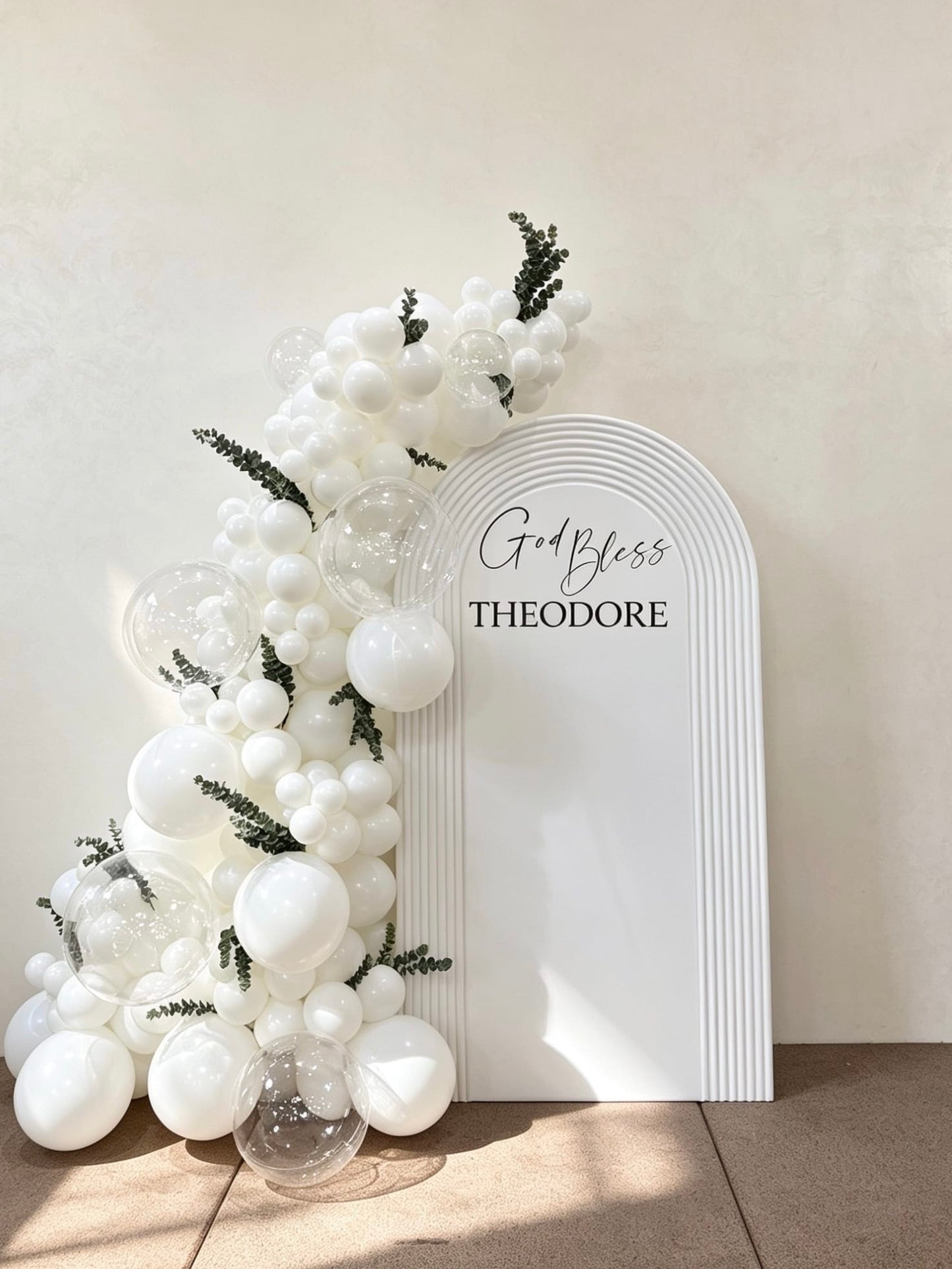 White communion ripple arch backdrop with white balloon garland and clear bubble balloons