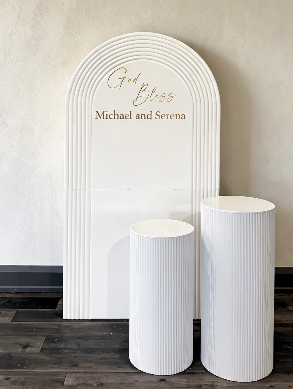 White ripple arch backdrop with custom lettering and two matching white pedestal stands.