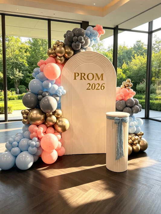 White ribbed prom backdrop with pastel blue, blush pink, dusk blue and gold balloon garland, custom prom lettering and matching white ribbed pedestal.