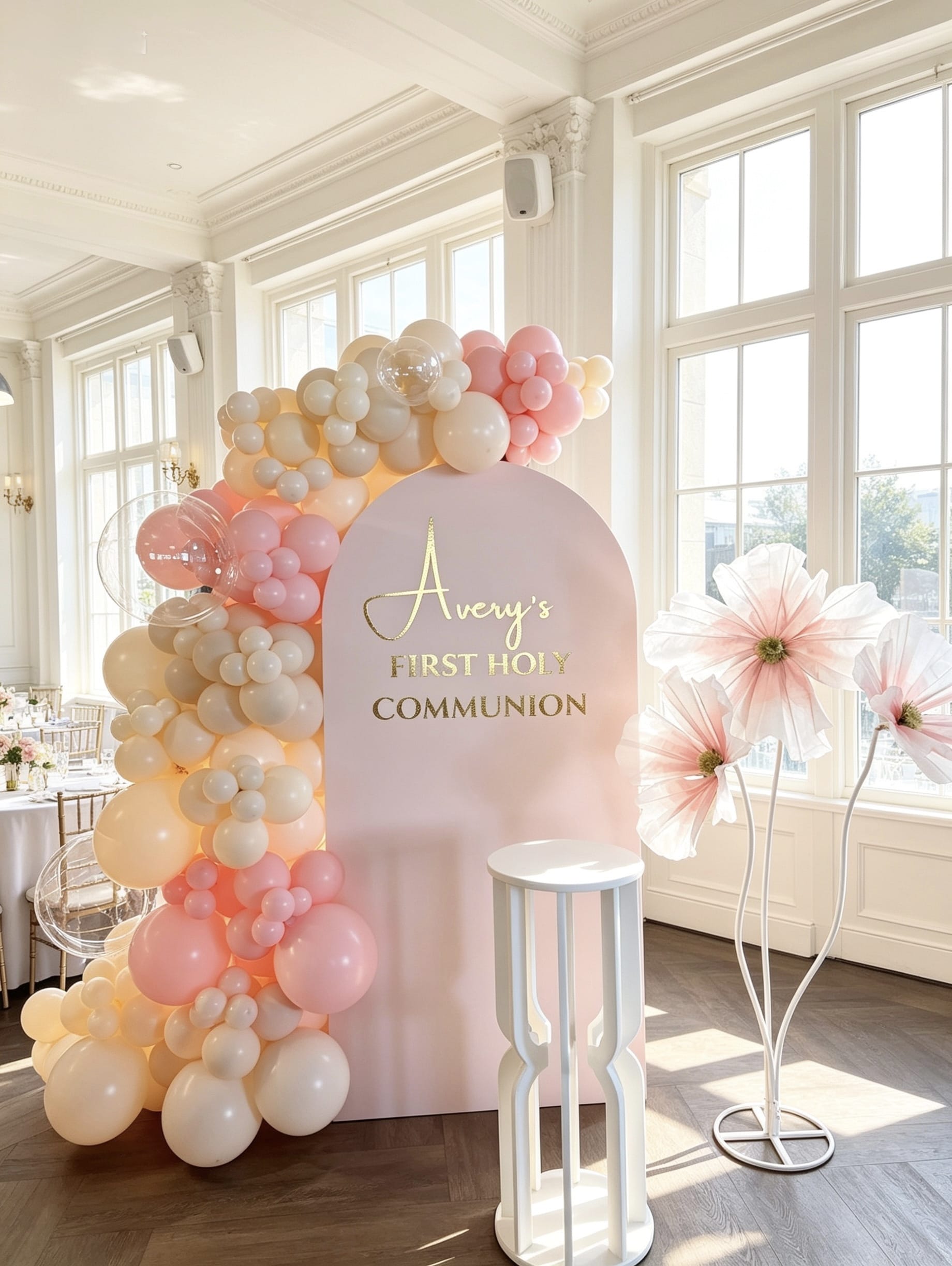 Blush pink First Holy Communion backdrop with organic balloon garland, clear bubble balloons, oversized floral props and custom gold lettering.
