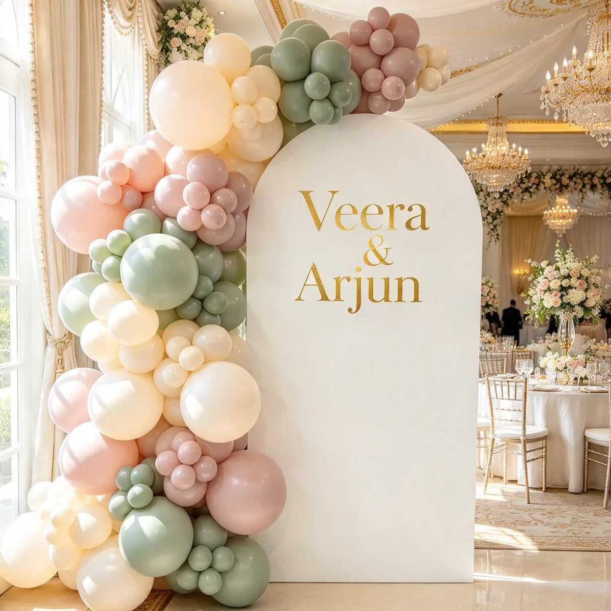 White wedding arch with gold couple’s names and an organic balloon garland in sage green, blush pink, dusty rose, and cream.