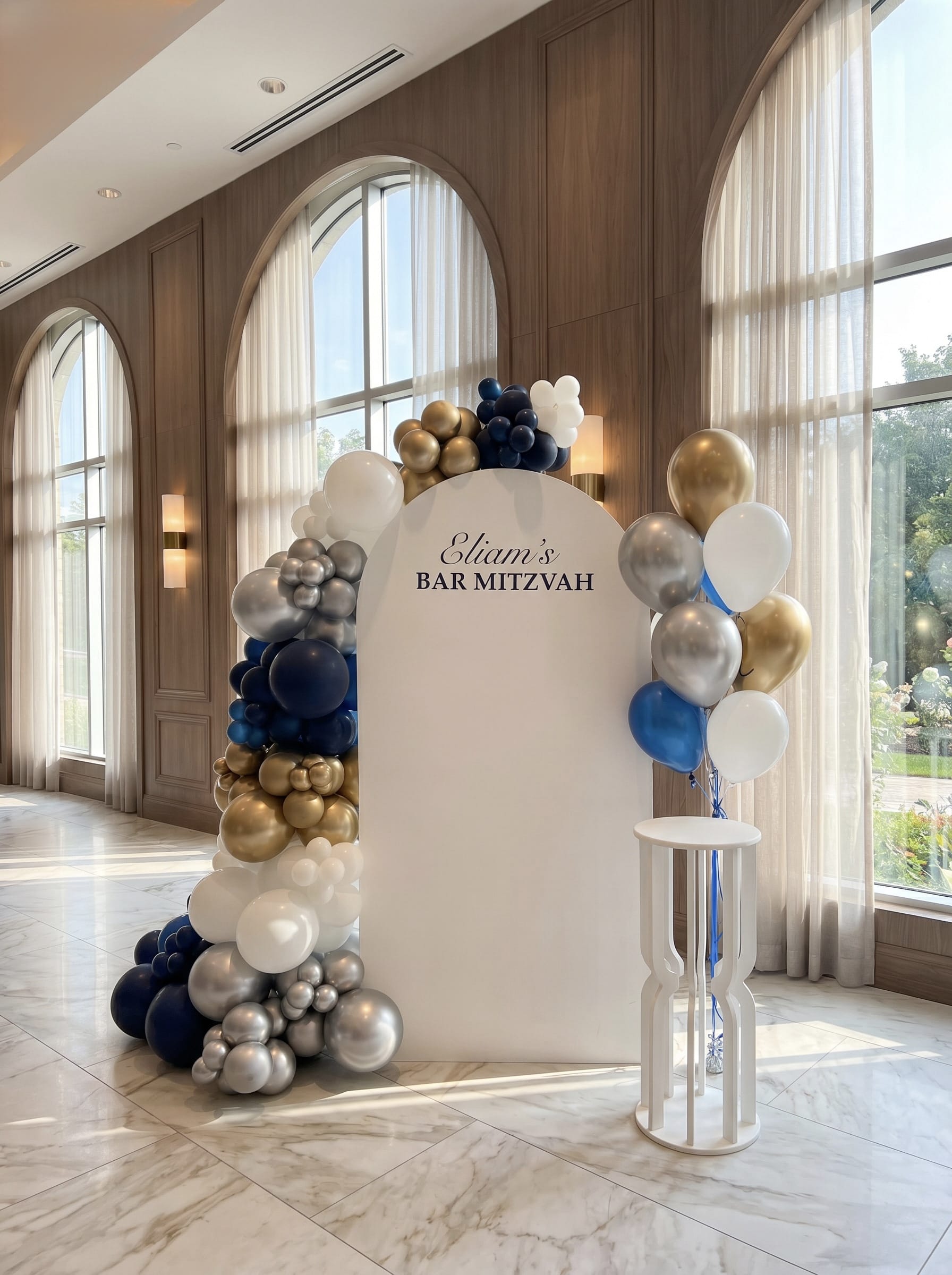 White Bar Mitzvah backdrop with navy, gold, silver and white balloon garland, custom name sign and matching helium balloon bouquet.