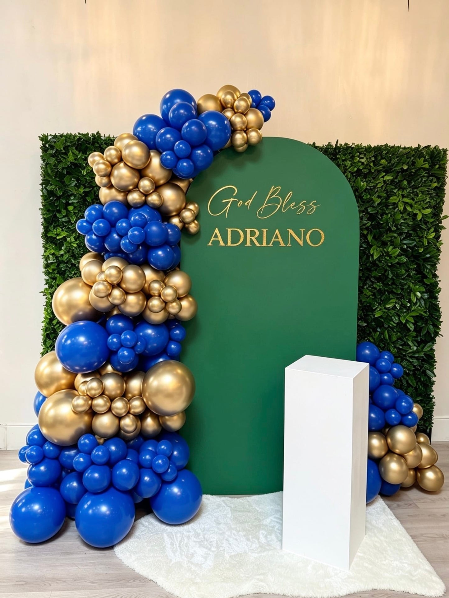 Green arch communion backdrop with royal blue and gold balloon garland, custom gold lettering and white cake pedestal