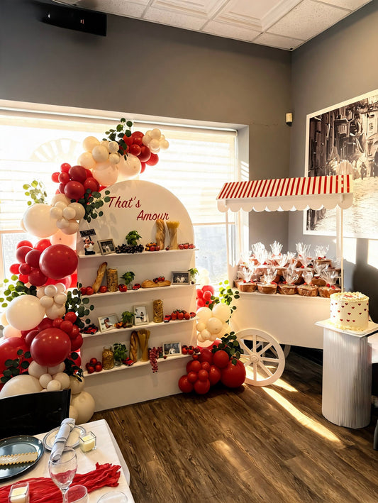 Italian market themed party display with red and white balloon garland, custom shelving, market cart and romantic celebration décor.