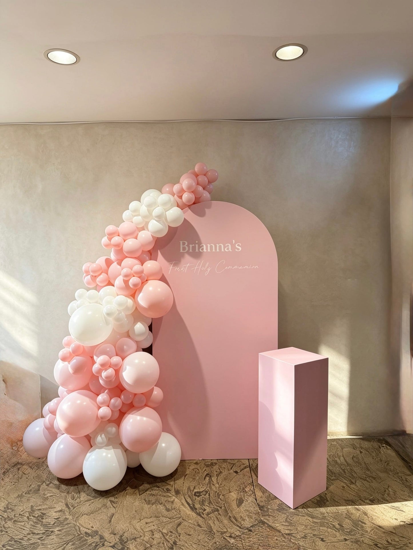 Blush pink communion backdrop with white and pink organic balloon garland and matching pedestal stand