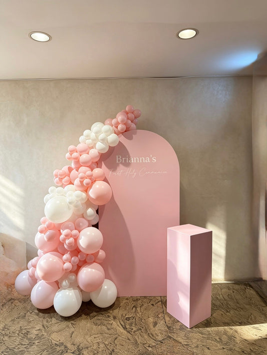 Blush pink communion backdrop with white and pink organic balloon garland and matching pedestal stand