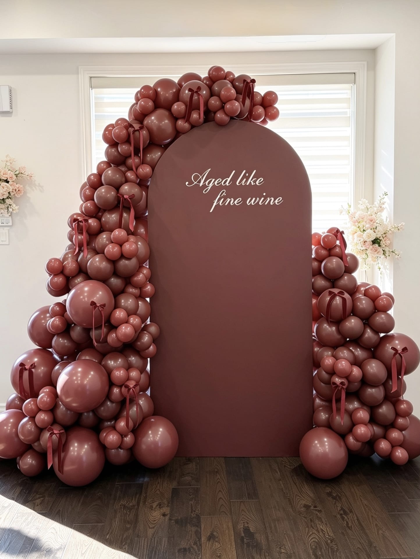 Burgundy birthday backdrop with matching balloon garland, ribbon accents and custom aged like fine wine lettering
