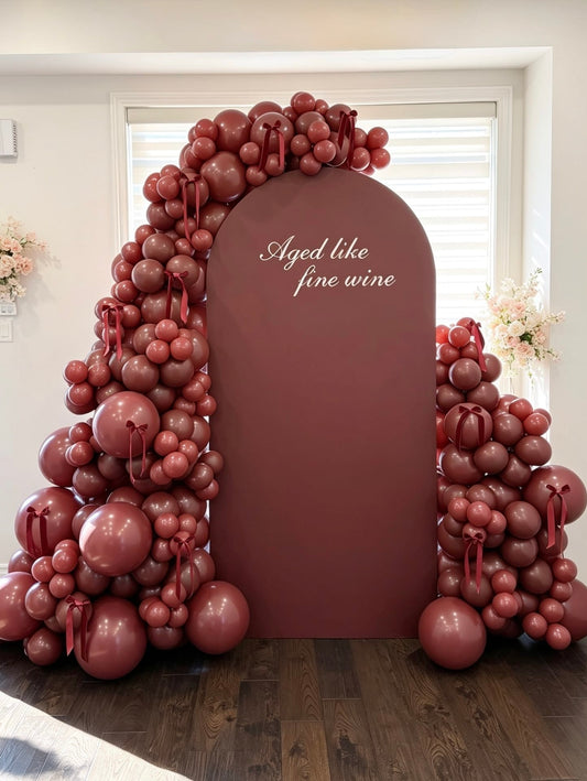 Burgundy birthday backdrop with matching balloon garland, ribbon accents and custom aged like fine wine lettering