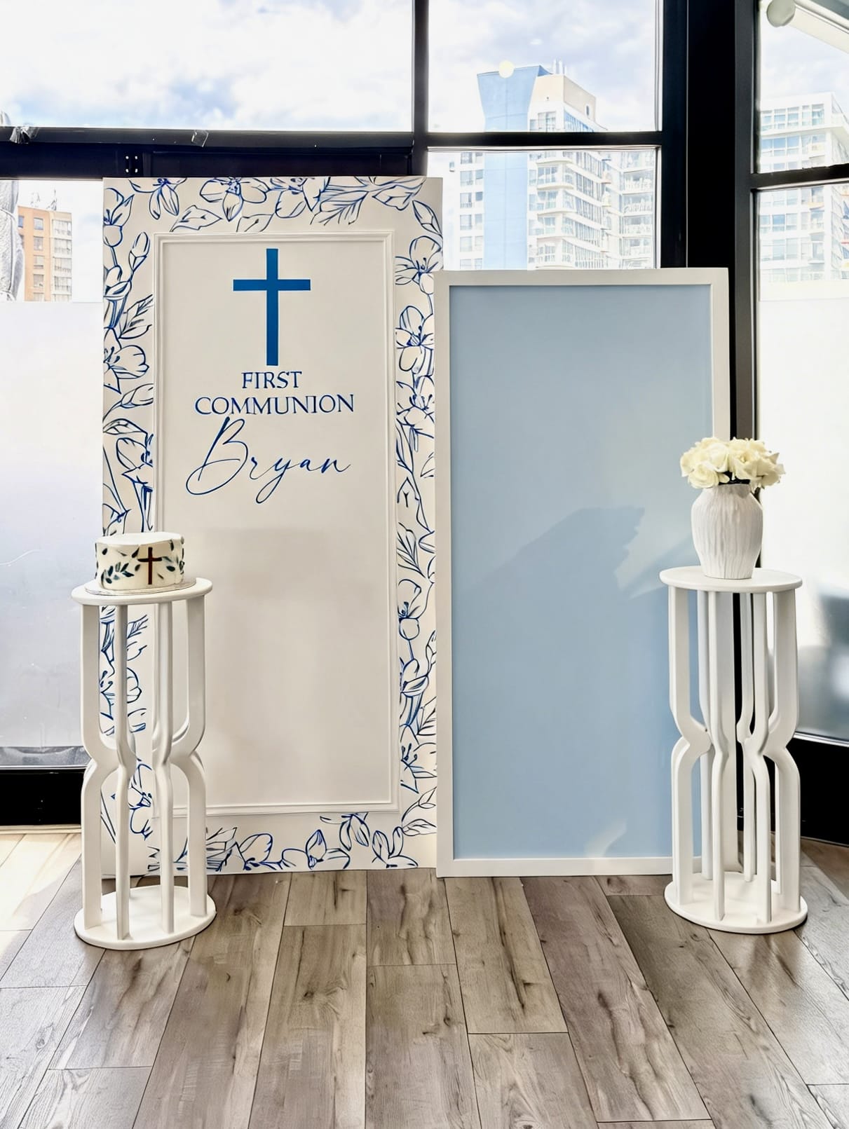 Blue and white first communion backdrop with floral frame design, custom name and matching pedestal stands.