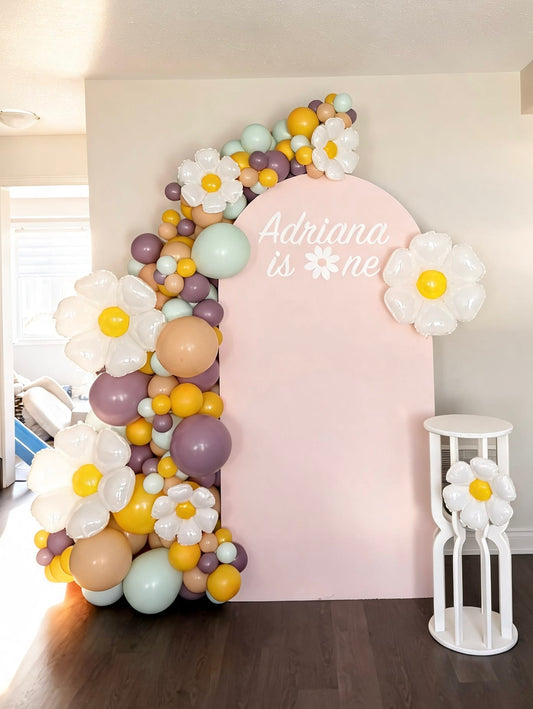 Pink daisy birthday backdrop with pastel balloon garland, oversized flower balloons and custom first birthday sign for a baby girl celebration.