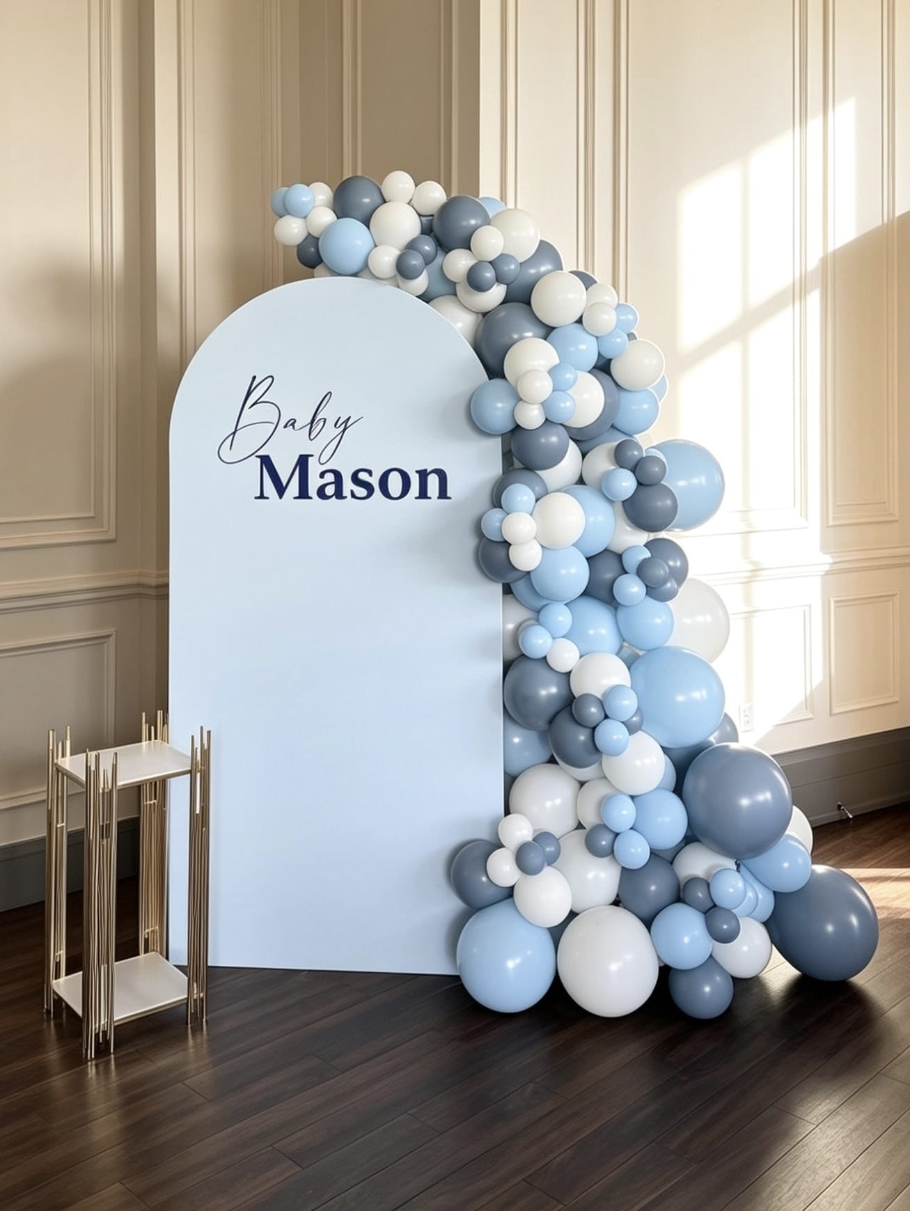 Baby blue shower backdrop with a soft blue arch, blue and white organic balloon garland, custom name sign and modern gold display stand.