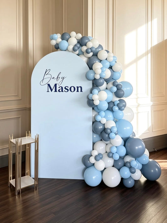 Baby blue shower backdrop with a soft blue arch, blue and white organic balloon garland, custom name sign and modern gold display stand.