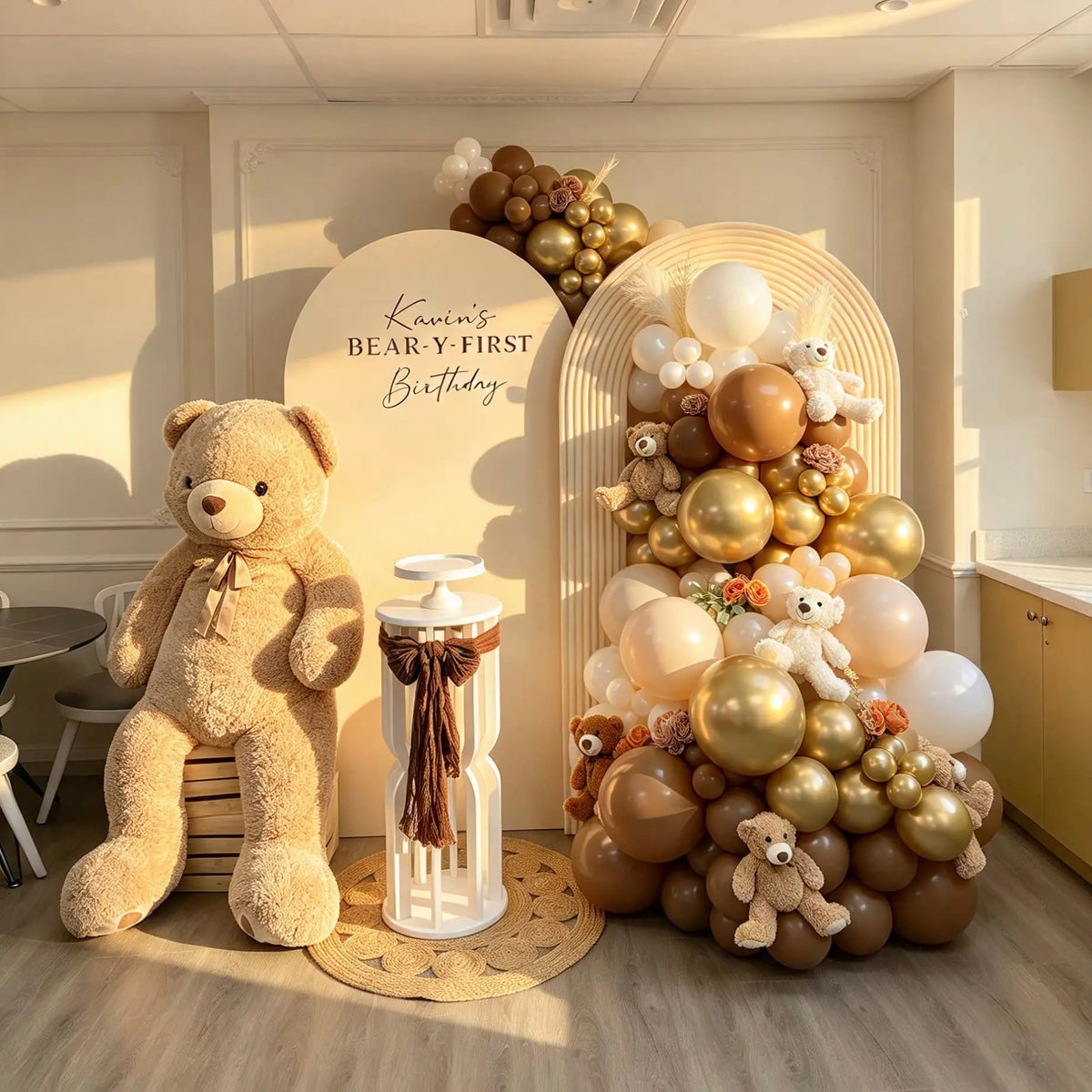 Cream birthday arches with brown and gold balloons, teddy bears, floral accents, and a white cake pedestal decorated with a brown bow.