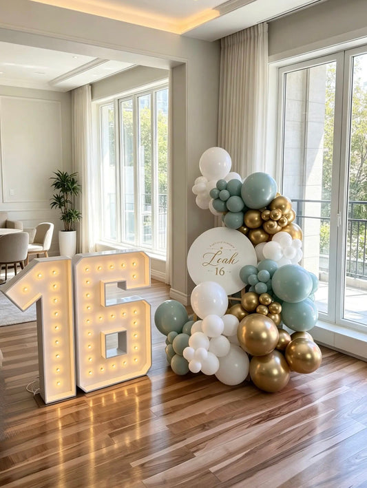 Sweet 16 birthday decor with illuminated marquee number 16, personalized round sign and sage green, white and gold balloon garland.
