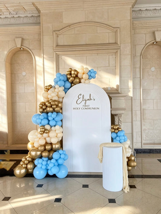 White ripple arch backdrop with blue, ivory and gold balloon garlands and custom First Holy Communion lettering.