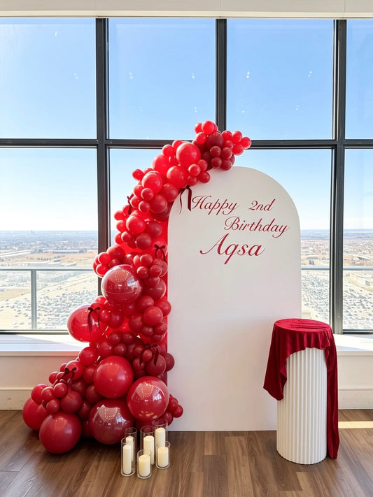 white full arch birthday backdrop with red monochrome balloon garland and ripple cake table