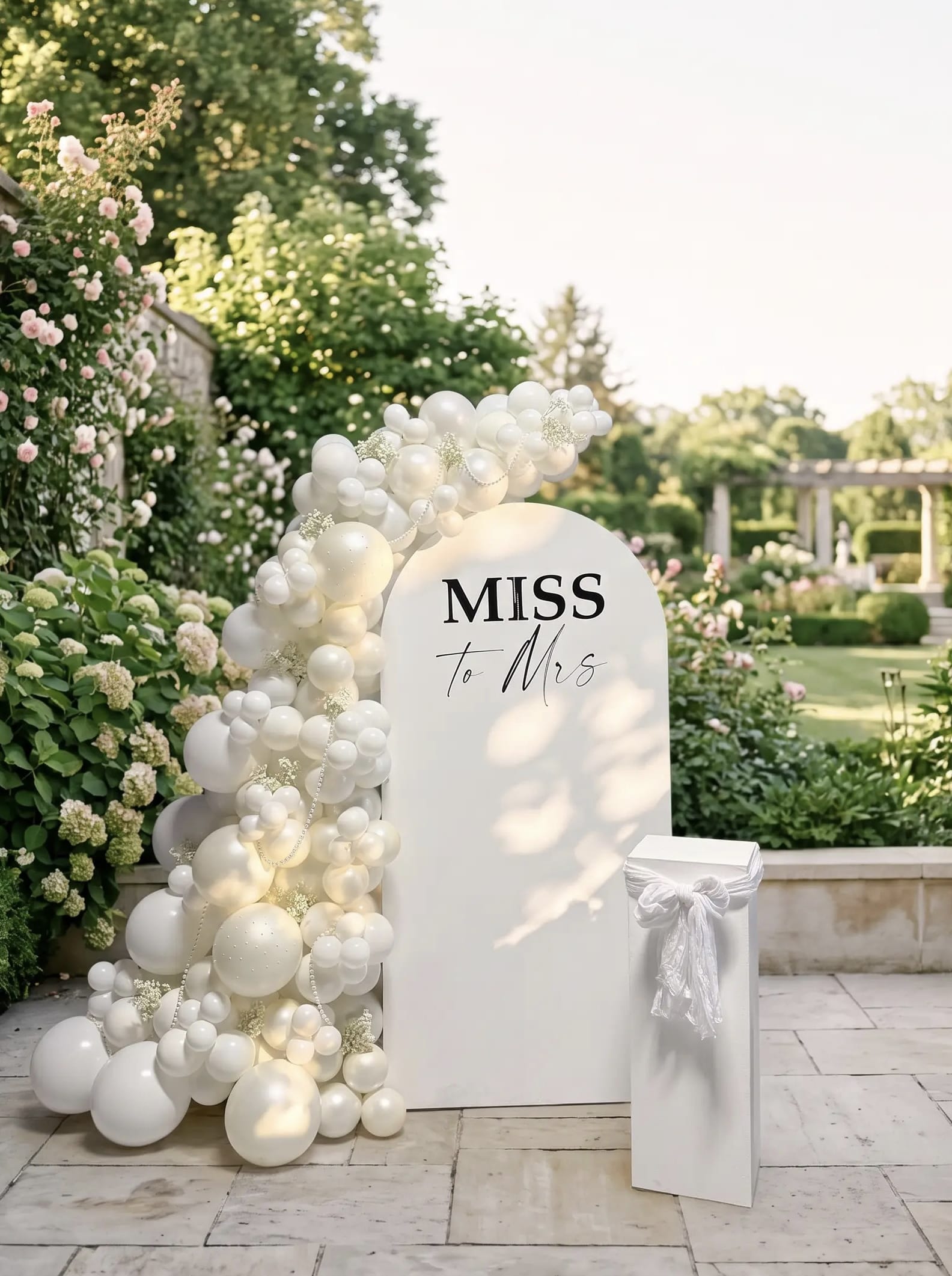 All-white Miss to Mrs bridal shower backdrop with an organic white balloon garland, pearl accents and a modern white pedestal.