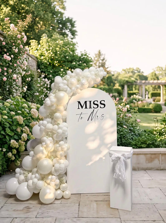 All-white Miss to Mrs bridal shower backdrop with an organic white balloon garland, pearl accents and a modern white pedestal.