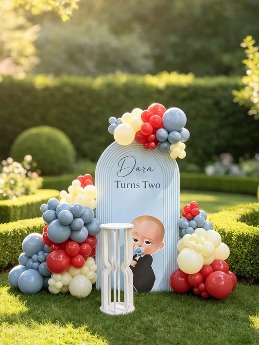Boss Baby birthday backdrop with character cutout, red, blue and ivory organic balloon arrangements and white cake table.