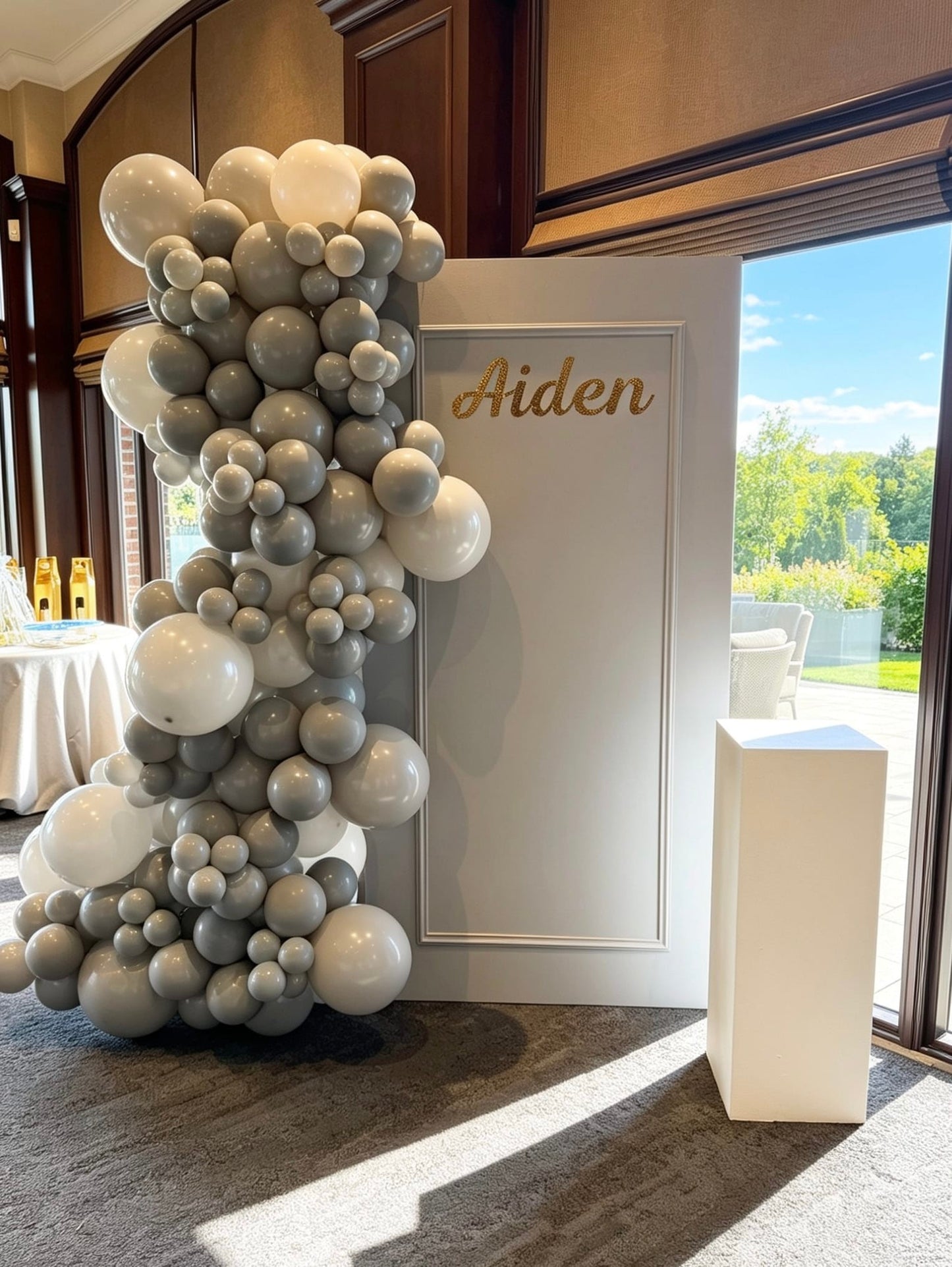Grey framed backdrop with grey and white balloon garland and custom gold name sign.