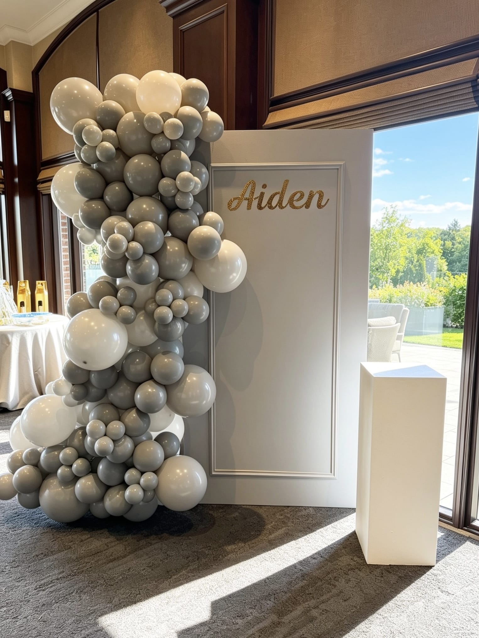 Grey framed backdrop with grey and white balloon garland and custom gold name sign.