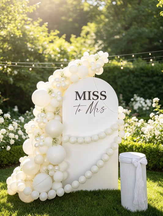 Elegant Miss to Mrs bridal shower backdrop with an ivory balloon garland, pearl garlands, baby’s breath accents, custom lettering and matching pedestal.