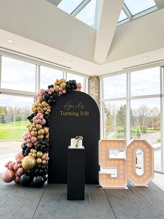 Black 50th birthday backdrop with illuminated marquee numbers, black, rose gold and gold balloon garland and custom lettering