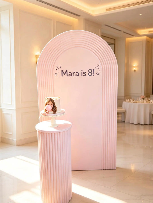 Pink birthday arch backdrop with personalized birthday sign and matching pink ribbed cake table.