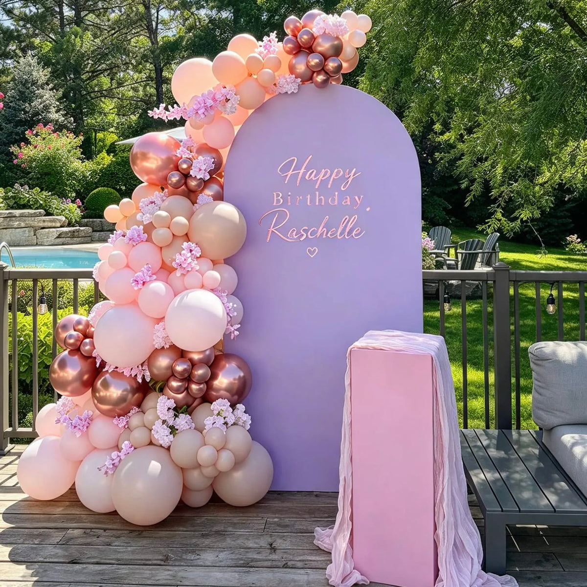 Lavender birthday arch with personalized lettering, blush and rose gold balloons, floral accents, and a draped pink cake pedestal.