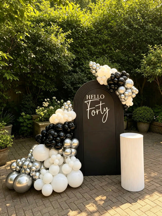  Black 40th birthday backdrop with Hello Forty sign, black, white and metallic silver balloon garland, and white ripple cake table.
