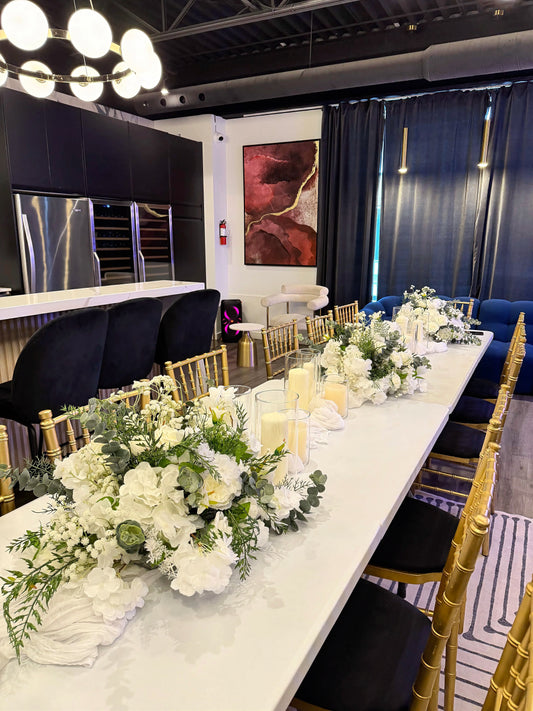 Elegant 12 ft table styling with white floral centerpieces, candles in glass vases and layered table runners