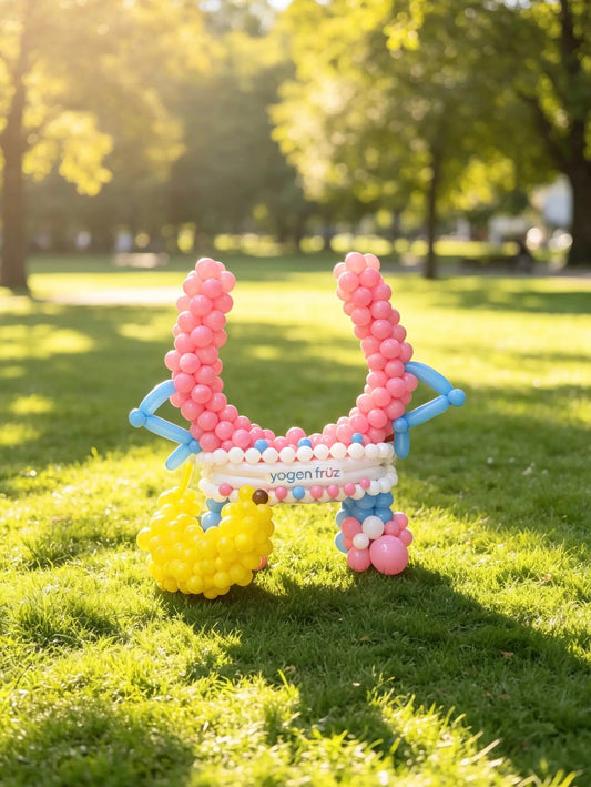 Custom pink balloon brand mascot sculpture with arms, legs, branded logo and yellow banana prop for a corporate brand activation