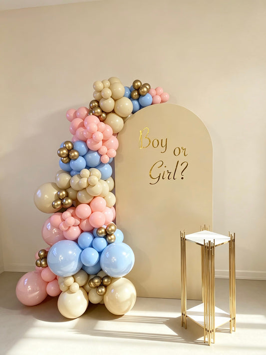 Gender reveal backdrop with pastel pink and blue balloon garland and gold accents
