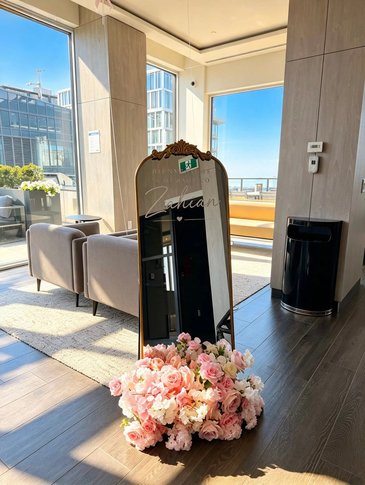 Ornate gold mirror welcome sign with personalized baptism lettering and a pink and white floral arrangement at the base.