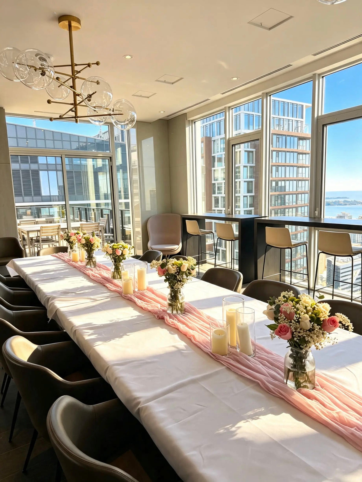 Long table with a white tablecloth, blush pink runner, pink and white floral centrepieces, and ivory candles in glass cylinders.