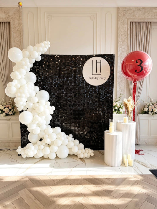 Black shimmer wall backdrop with white balloon garland, custom sign panel, white plinths and jumbo helium birthday balloon