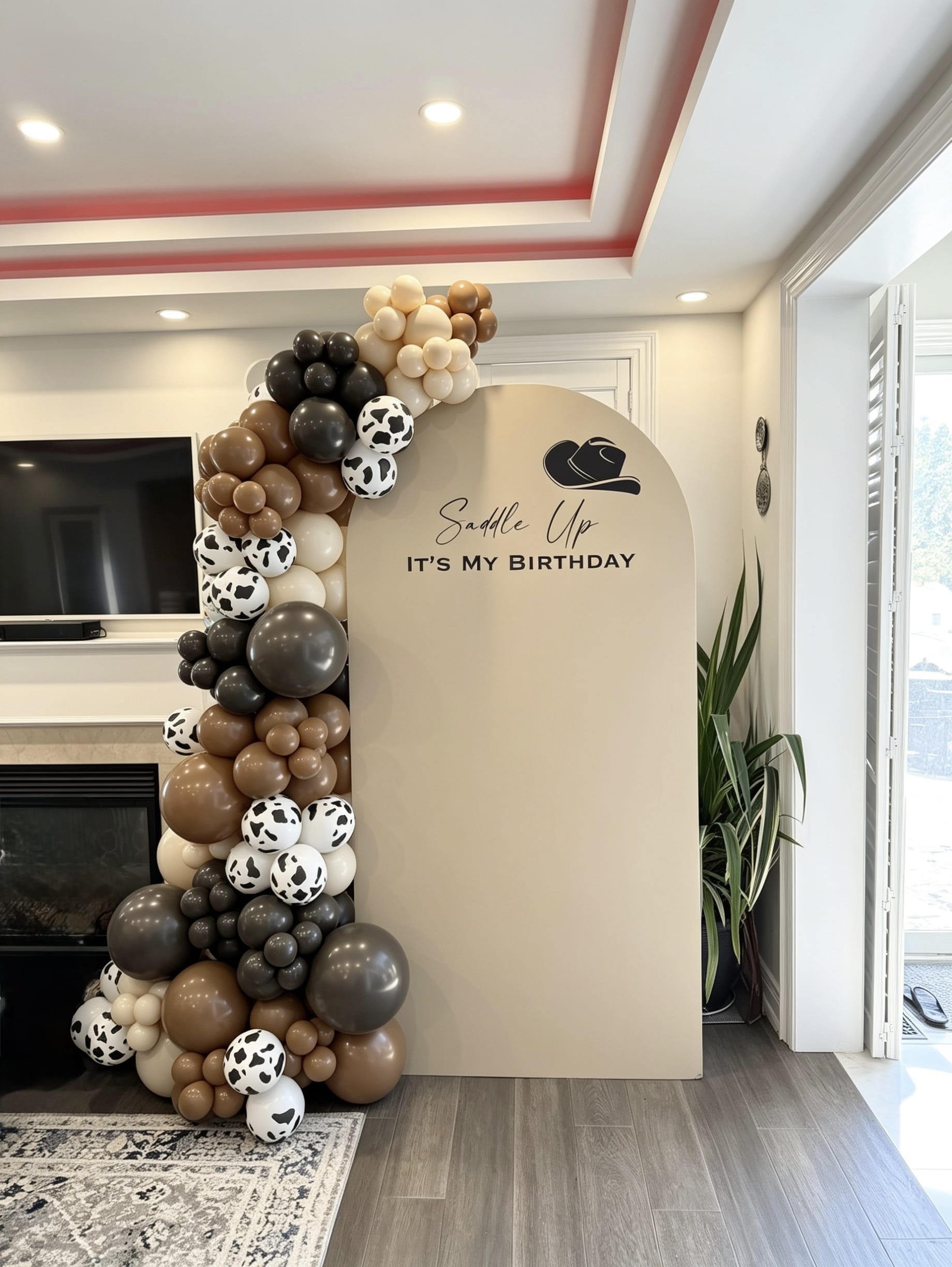 western cowboy birthday backdrop with brown balloon garland and cow print balloons