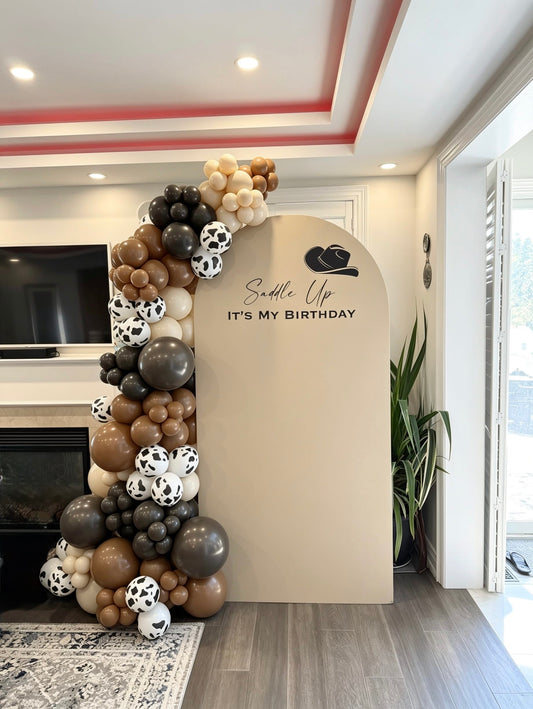 western cowboy birthday backdrop with brown balloon garland and cow print balloons
