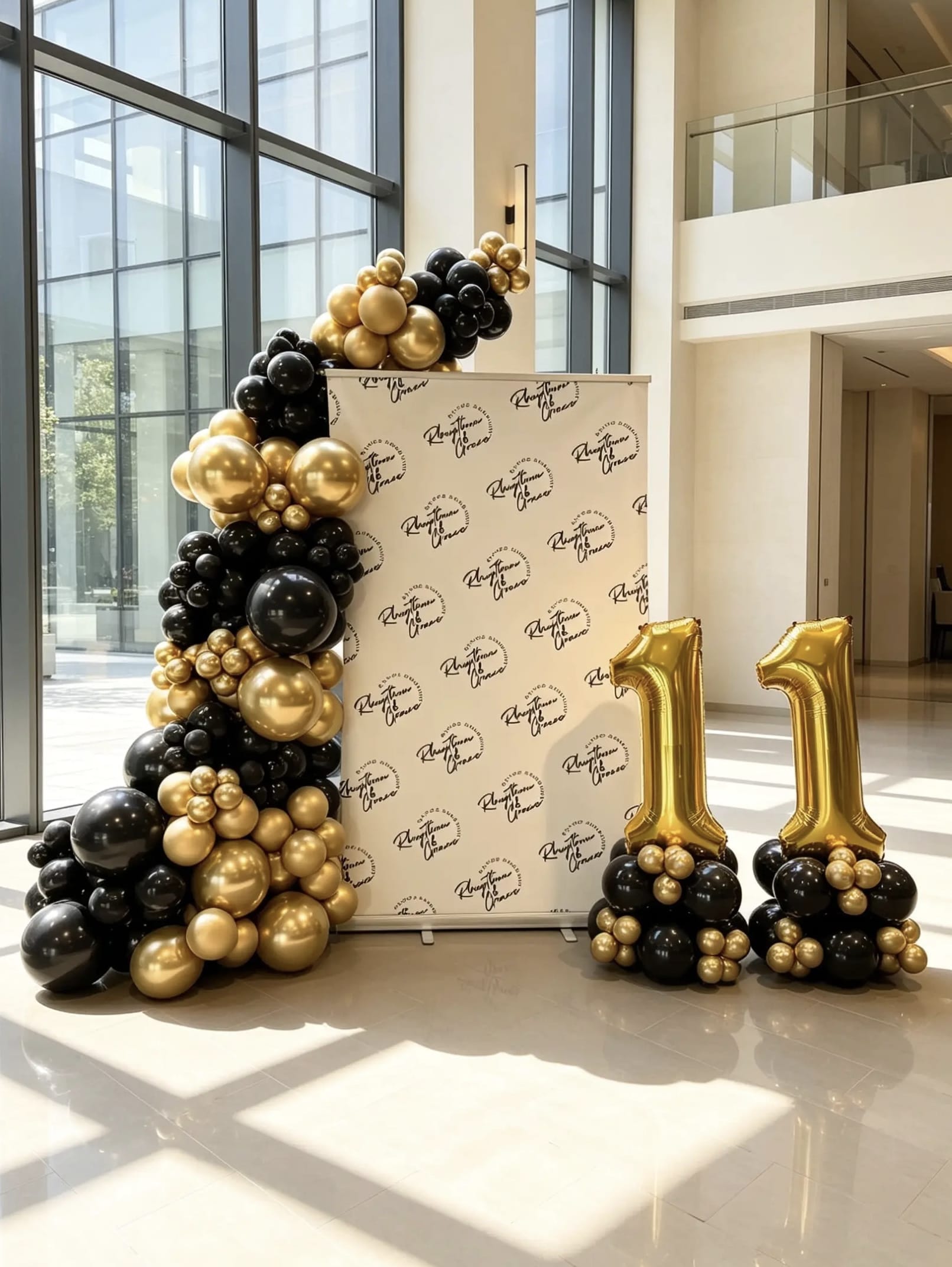 Corporate step and repeat backdrop with a black and metallic gold balloon garland and matching jumbo foil number balloons.