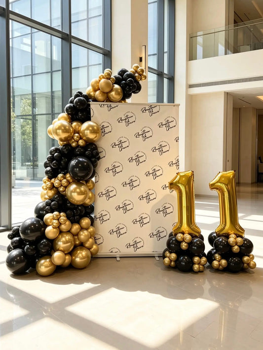 Corporate step and repeat backdrop with a black and metallic gold balloon garland and matching jumbo foil number balloons.