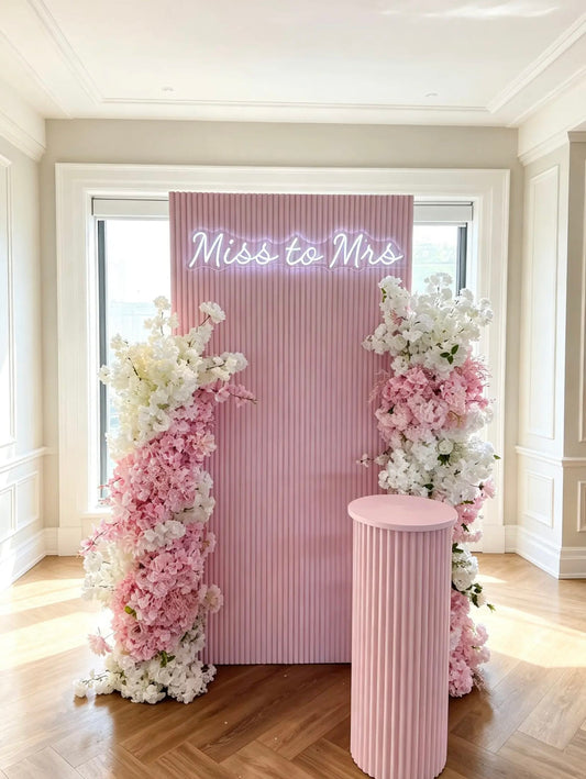 Pink Miss to Mrs bridal shower backdrop with white and blush floral arrangements, neon sign, and pink ripple cake table.