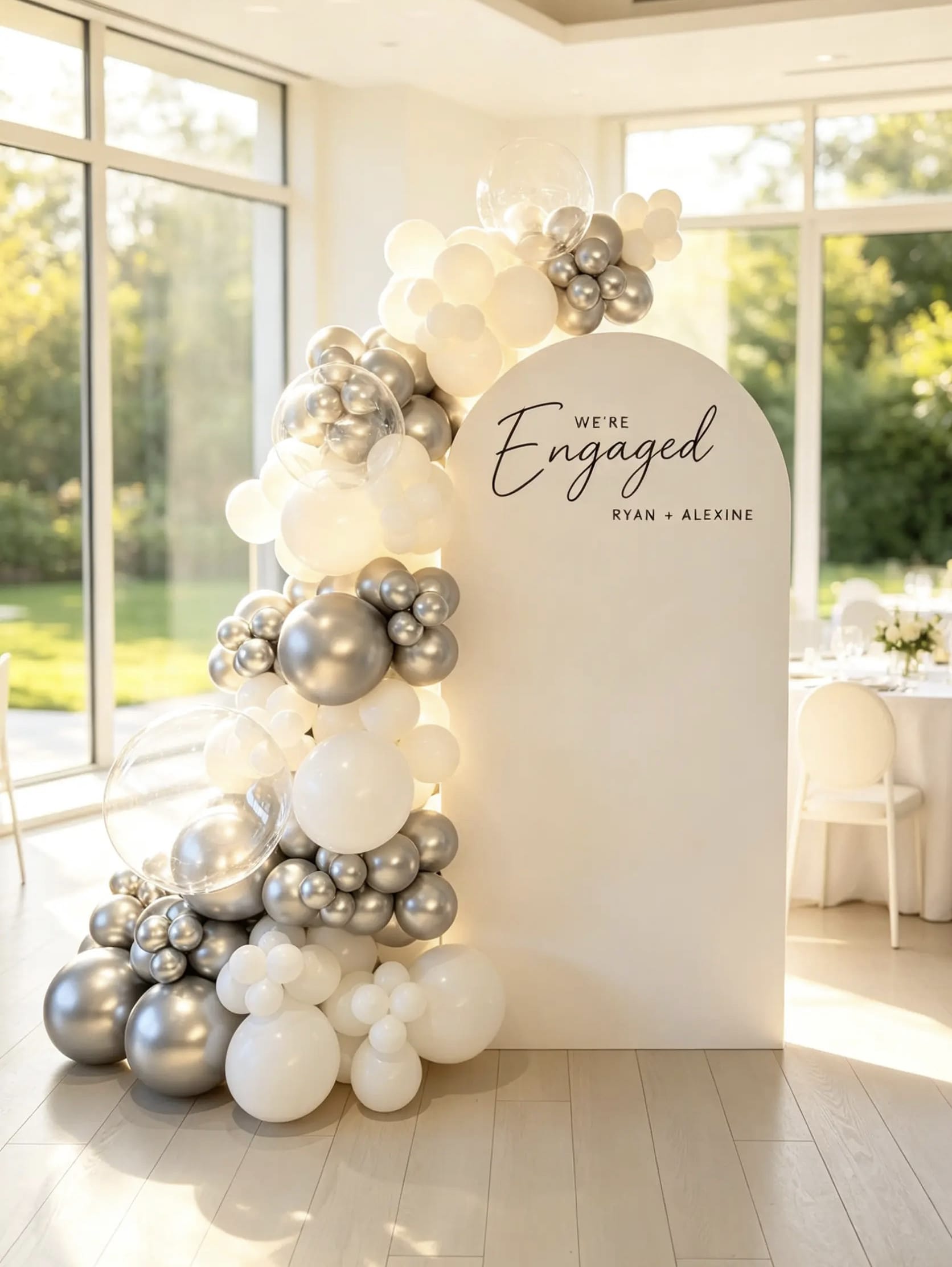 Engagement backdrop with white arch, personalized names, white and metallic silver balloon garland and clear bubble balloons.