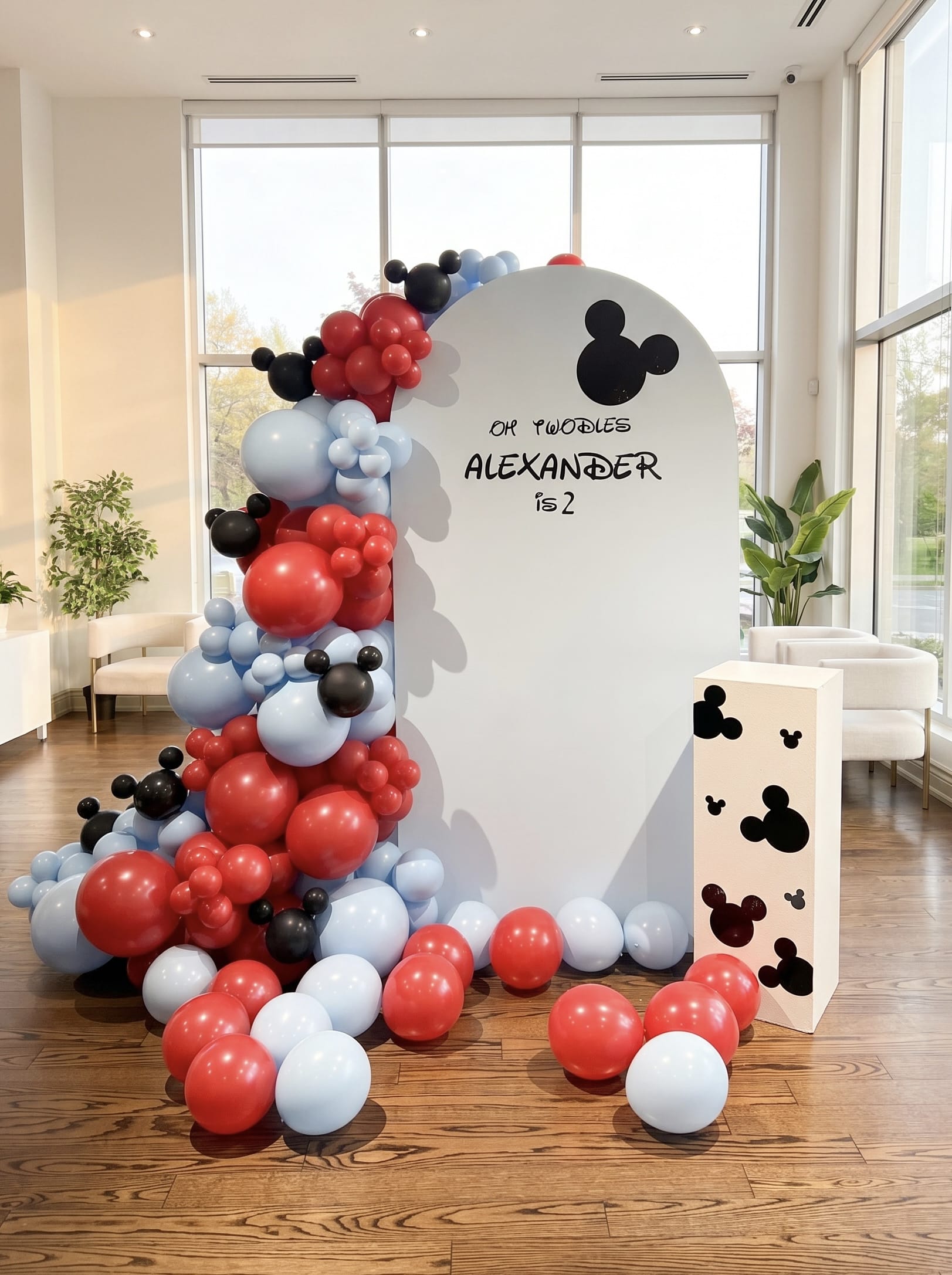 Oh Twodles second birthday backdrop featuring a white arch panel, red, black and pastel blue balloon garland, themed mouse accents and custom name personalization.
