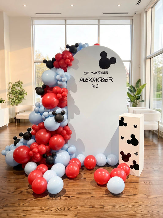 Oh Twodles second birthday backdrop featuring a white arch panel, red, black and pastel blue balloon garland, themed mouse accents and custom name personalization.