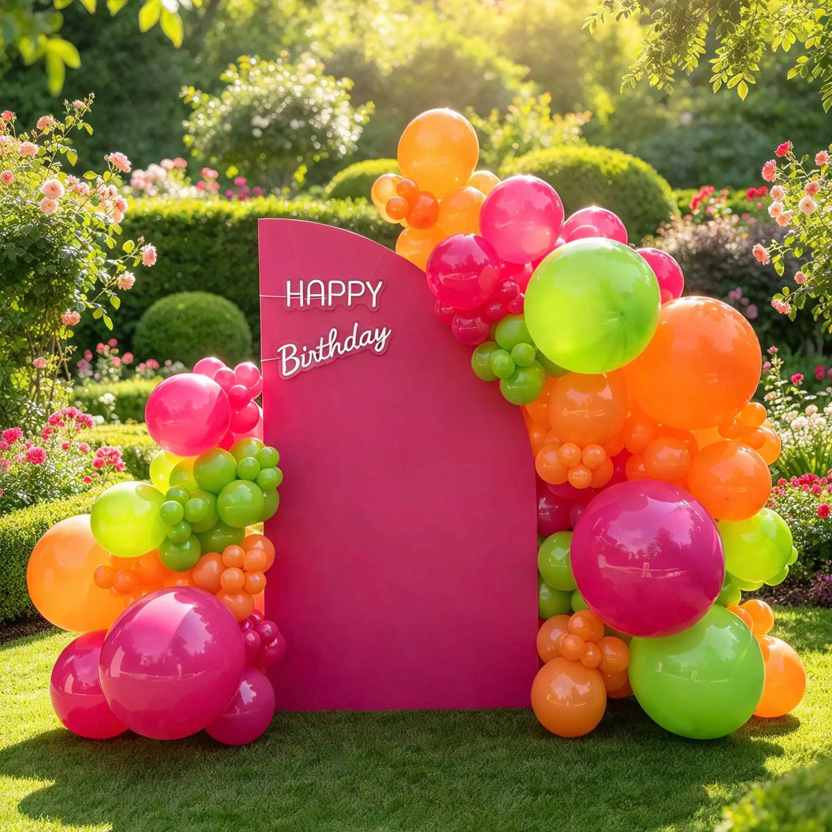 Hot pink birthday backdrop with a white “Happy Birthday” sign and vibrant pink, orange, and lime green balloon arrangements outdoors.