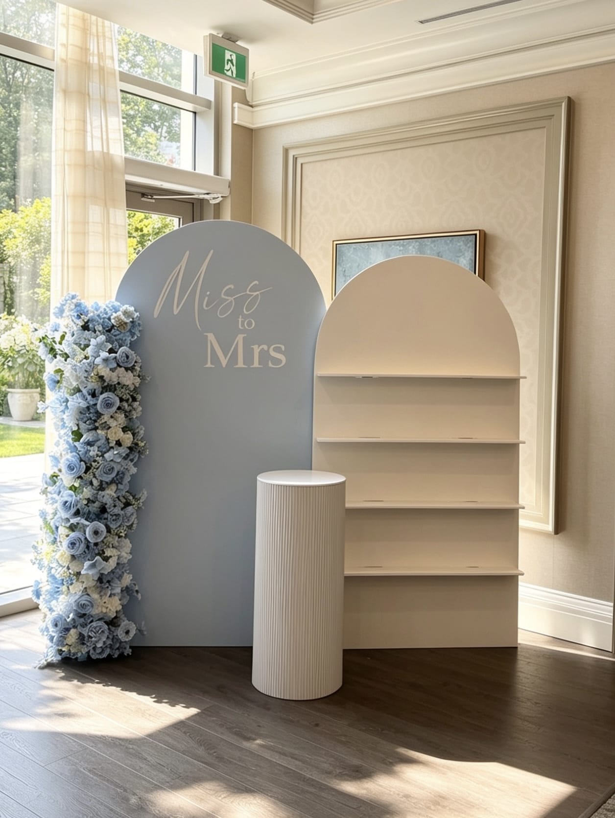 Blue Miss to Mrs backdrop with champagne wall shelving, floral styling and white pedestal stand.