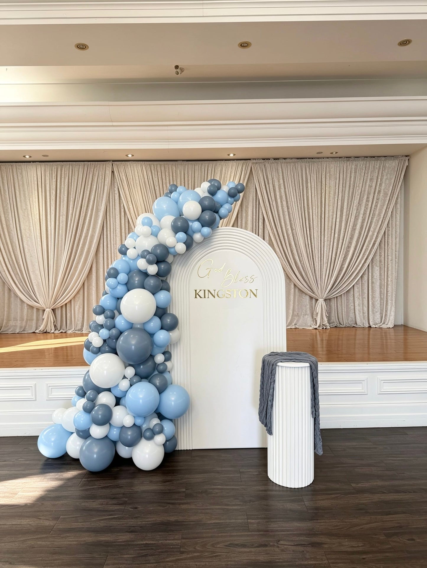 White ripple arch communion backdrop with blue and white balloon garland and matching cake pedestal